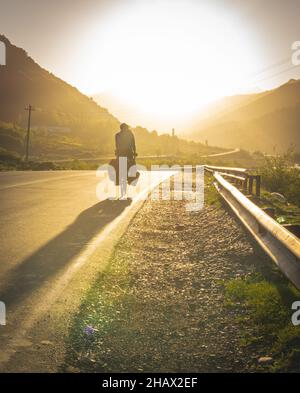 Person auf beladenem Fahrrad passiert georgische Straßenschild mit Bergen vor. Reisen Sie in Georgien Nationalpark und kaukasus Berge.Vertikal backgr Stockfoto