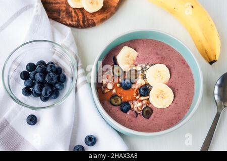 Geglättet mit Banane, Chiasamen, Heidelbeeren, Nüssen und Erdnussbutter. Veganes Frühstück. Draufsicht, flach liegend Stockfoto