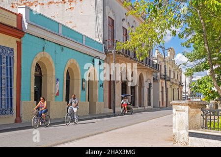 Bicitaxi / Fahrradtaxi und Kubaner radeln durch die Straße mit Gebäuden im spanischen Kolonialstil in der Altstadt der Stadt Camagüey, Kuba Stockfoto