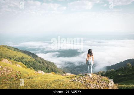 Solo Brünette Frau entspannt steht am Rand über Wolken unbeschwerten Lebensstil. Abenteuer und Erfüllung im Lebenskonzept. Stockfoto