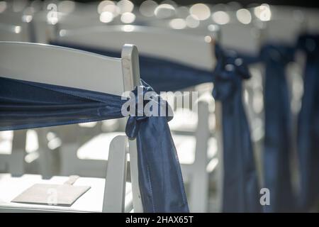 Weiße Hochzeitsstühle in Insel mit blauen Schleifen und Bändern Stockfoto