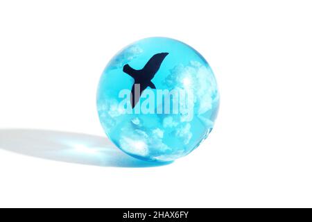 Kleine blaue Kugel aus Glas mit Wolken und einem fliegenden Vogel im Inneren isoliert auf Weiß Stockfoto