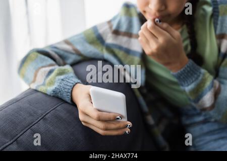 Beschnittene Ansicht eines verschwommenen afroamerikanischen Teenagers, der zu Hause auf dem Handy chattet Stockfoto