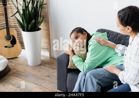 Verschwommene afroamerikanische Mutter beruhigend verärgert Tochter umarmt Kissen und wegschauen Stockfoto