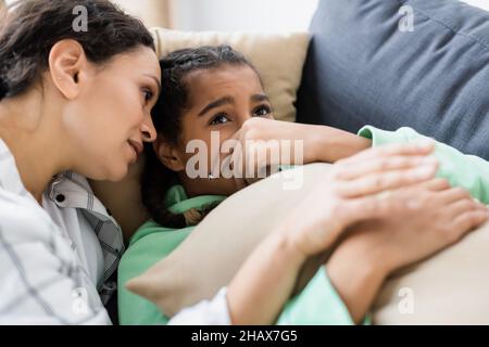 afroamerikanische Frau beruhigt verärgert Tochter auf Couch liegen und verdunkeln Gesicht mit der Hand Stockfoto