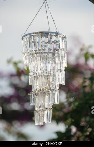 Kristallleuchter, der im Freien mit rosa und grünen Blättern im Hintergrund hängt Stockfoto
