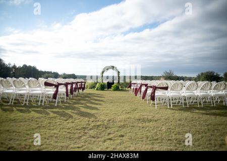 Weiße Hochzeitsstühle in Insel mit roten Schleifen und Bändern Stockfoto