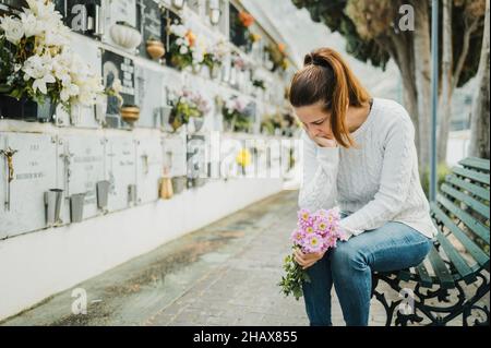 Weinende Frau witting auf der Bank in der Nähe der Grabmauer auf dem Friedhof Stockfoto