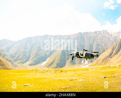 Kommerzielle Drohne über dem Boden mit gelbem Gras unten und Berg im Hintergrund. Sicherheitsbestimmungen für das Pilotieren von kommerziellen Drohnen und Videoaufnahmen Stockfoto