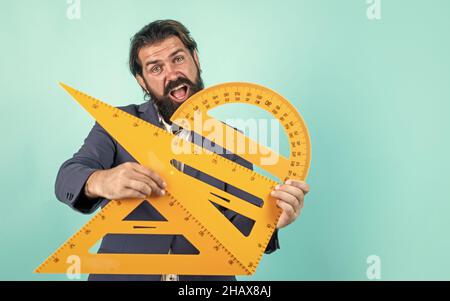 Bestehen Sie die Mathe-Prüfung. Lernen Sie das Thema. Glücklicher Mann mit Bart mit Dreieck und Winkelmesser. Studium der Messung. Formale Bildung. Männlicher Student Stockfoto