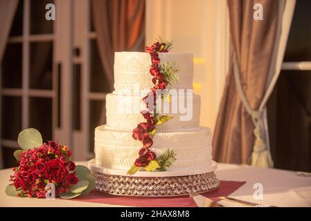 Wunderschöne dreistufige weiße Hochzeitstorte mit roten Blumen Dekoration beim Hochzeitsempfang Stockfoto