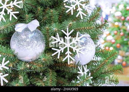 Weiße Schneeflocken und schneebedeckte Weihnachtskugeln auf dem Weihnachtsbaum. Stockfoto