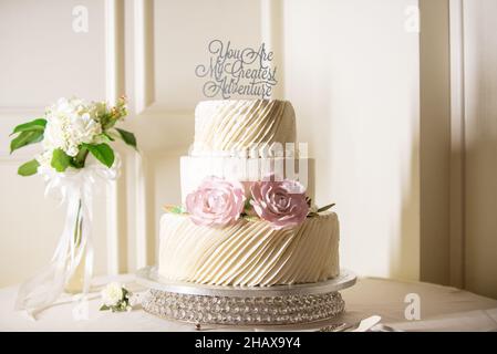 Wunderschöne weiße dreistufige Hochzeitstorte mit „You are my greatest Adventure“-Kuchenform Stockfoto