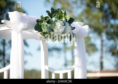 Weißer Hochzeitsbogen mit weißem Tuch und Plue und weißen Blumen Stockfoto