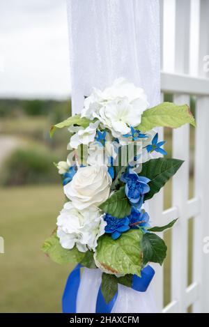 Weißer Hochzeits-Bogen mit weißem Tuch und weißen und blauen Blumen geschmückt Stockfoto