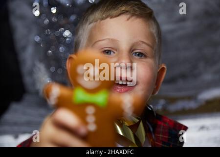 Liebenswert glücklich kaukasischen Kind mit Lebkuchen und macht einen lustigen Gesichtsausdruck. Selektiver Fokus. Stimmungsvolles, ästhetisches Weihnachtshaus für Neujahr Stockfoto