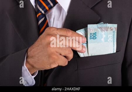 Ein Geschäftsmann hält brasilianisches Geld in der Hand in seiner Tasche. Stockfoto