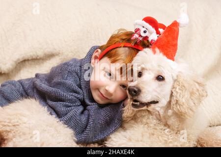 Ein kleiner Junge umarmt einen großen Hund in Weihnachtsmützen. Wir feiern Neujahr, weihnachten Stockfoto