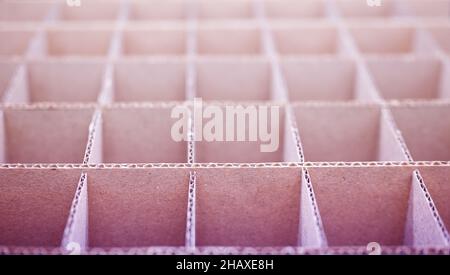 Abstrakter Hintergrund. Quadratische Trennwände aus Pappe aus nächster Nähe. Trennwände für den Transport empfindlicher Glasgegenstände. Geringe Schärfentiefe, rosa getönt. Stockfoto