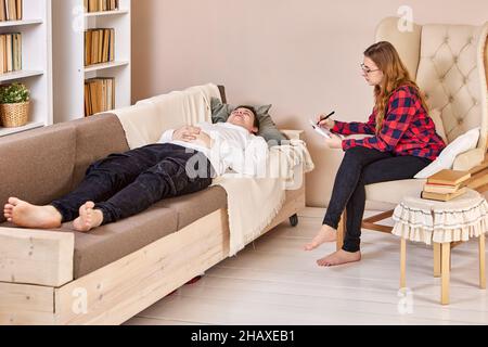 Psychotherapeut, der im Heimbüro arbeitet, Mann, der während eines Termins auf der Couch liegt. Stockfoto