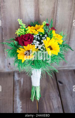 Wunderschöne Sonnenblumen- und rote Rosen-Brautsträuße auf Holzvertäfelung Stockfoto