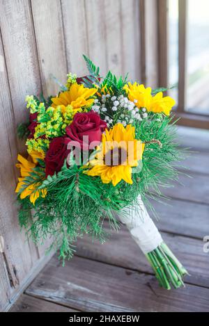 Wunderschöne Sonnenblumen- und rote Rosen-Brautsträuße auf Holzvertäfelung Stockfoto