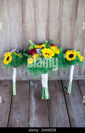 Wunderschöne Sonnenblumen- und rote Rosen-Brautsträuße auf Holzvertäfelung Stockfoto