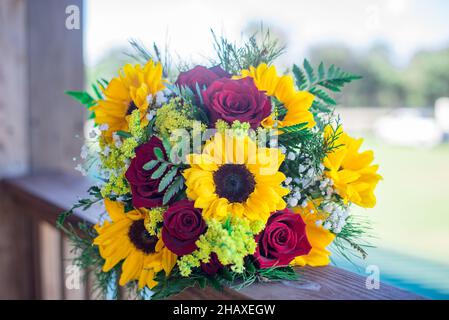 Wunderschöne Sonnenblumen- und rote Rosen-Brautsträuße auf Holzvertäfelung Stockfoto