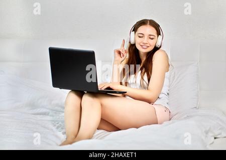 Eine Frau mit Kopfhörern und einem Laptop im Bett bedeckte ihre Augen. Stockfoto