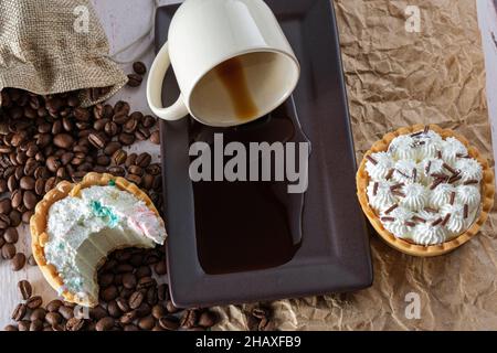 Mini-Ganache aus weißer Schokolade mit einem Biss, neben einer Tasse Kaffee, der auf braunem Papier umgedreht wurde. Stockfoto