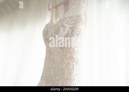 Wunderschöne weiße Bräute Kleid hängen vom Fenster mit weißen Vorhängen Stockfoto
