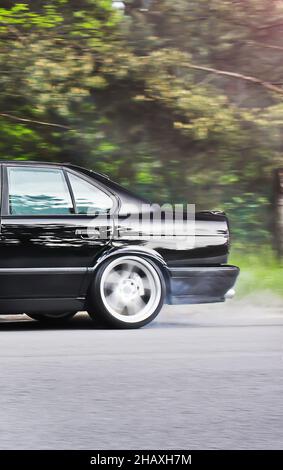 Teil eines alten schwarzen Autos auf dem Hintergrund der Straße und Bäume Stockfoto