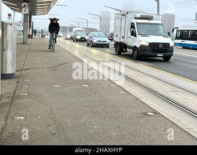 Mann, der in Zürich in der Schweiz auf einer mit Lichtern markierten Fahrradspur auf dem Boden Fahrrad fährt. Parallel gibt es Schienen für die Straßenbahn und befahrene Straße für Autos. Stockfoto