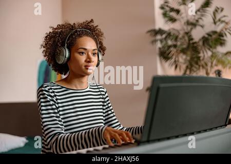 Frau in Kopfhörern spielt Synthesizer zu Hause Stockfoto