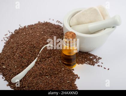 Braune Leinsamen, Leinöl, Keramiklöffel und Mörser mit Stößel. Stockfoto