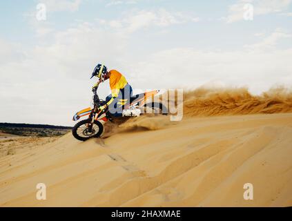 Professioneller Motocross-Fahrer, der den Sandberg hinunterrutscht Stockfoto