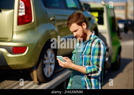 Mann ruft an, während der Abschleppwagen das Auto abholt Stockfoto