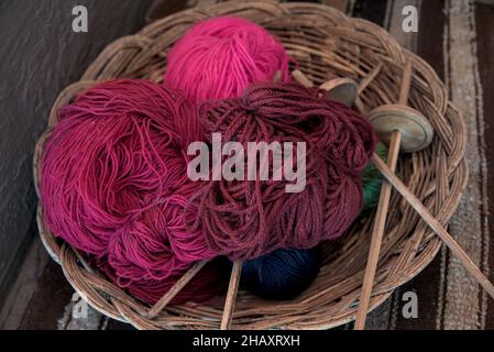Dyed alpaca llama wool in balls with traditional knitting needles resting in wicker bowl basket at peruvian textile farm for tourists to see ancient m Stockfoto