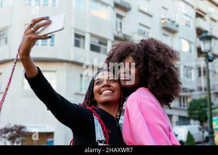 Sorglose afroamerikanische Freundinnen mit Afro-Frisuren, die auf dem Smartphone auf der Straße in der Stadt Selbstporträt machen Stockfoto