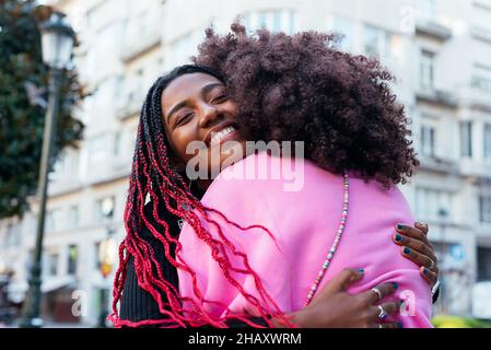 Junge fröhliche afroamerikanische Freundinnen umarmen sich gegenseitig auf der Straße Stockfoto