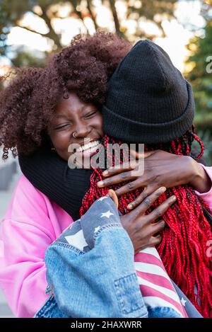 Junge, fröhliche afroamerikanische Freundinnen umarmen sich im Park Stockfoto
