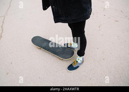 Von oben Crop anonyme Skater in schwarzen Jeans und Sneakers in der Nähe von Skateboard auf Asphalt Bürgersteig in der Stadt stehen Stockfoto