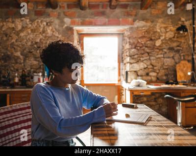 Hispanische Juwelierin sitzt am Tisch und versucht an Ringen, die in der Licht-Werkstatt auf weißer Plakette angebracht sind Stockfoto