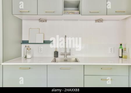 Interieur der modernen Küche mit hellgrünen Schränken und Schränken Waschbecken mit Wasserhahn und Metall Stockfoto