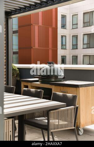 Außenansicht einer hellen, modernen Veranda mit Esstisch und einem tragbaren, eingebauten Grill im Tisch auf Rädern Stockfoto