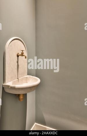 Weißes Marmorwaschbecken und vintage bronzefarbener Wasserhahn, an der grauen Wand im Badezimmer montiert Stockfoto