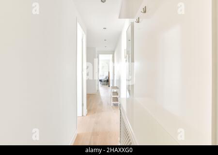 Interieur von Licht schmalen Flur mit weißen Wänden und Türen mit Regalen auf Parkettboden in modernen Wohnung platziert eingerichtet Stockfoto