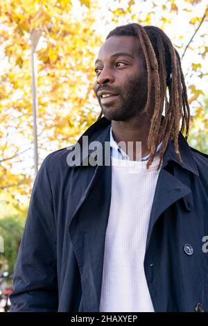 Fröhlicher afroamerikanischer Rüde in marineblauer Jacke und Dreadlocks im Stadtpark bei Tageslicht Stockfoto