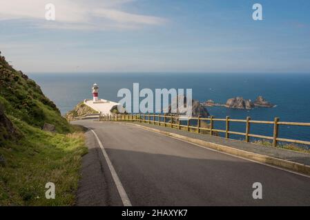 Malerische Drohnenansicht Asphaltstraße, die zum Cape Ortegal Leuchtturm führt, auf felsigen grünen Klippen gegen blaues Meer unter bewölktem Himmel platziert Stockfoto