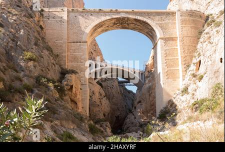 Hohe, steingealterte Brücken mit gewölbten Passagen zwischen felsigen Bergen und blauem Himmel in der sonnigen Natur Spaniens Stockfoto